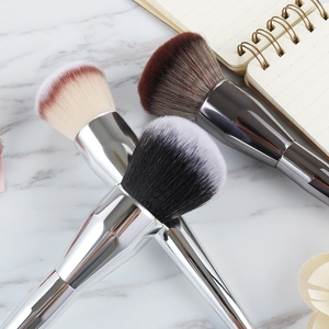 Three professional large makeup brushes with metallic handles on marble surface