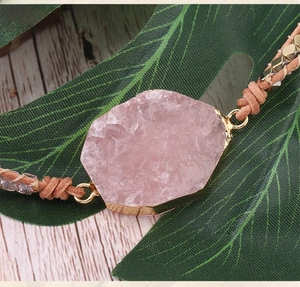 Detail of rose quartz stone with gold plating on a handmade brown braided cord bracelet