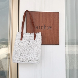 Close-up of white floral lace tote bag with brown leather straps hanging on a wooden wall