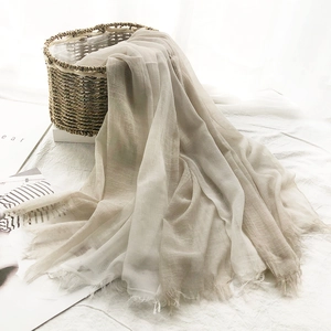 Lightweight beige linen scarf with fringe edges draped elegantly from a woven basket