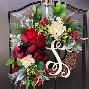 Christmas wreath with red and white flowers, plaid bow, and berries on a dark wooden door