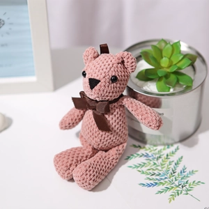 Pink handmade crochet teddy bear plush toy with brown bow in a cozy setting