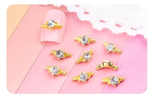 Détail de bijoux d'ongles dorés avec strass sur ongles roses et fond de dentelle blanche