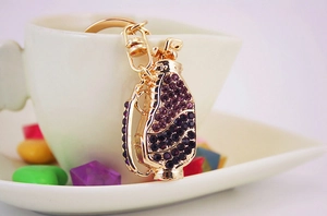 Detail of a gold golf bag keychain with purple rhinestones hanging on a white ceramic cup