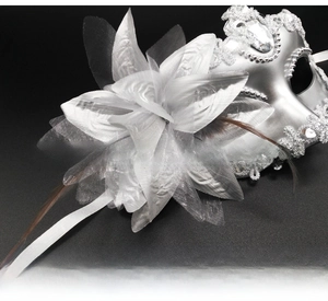Detailed close-up of a silver Venetian masquerade mask with white lace flower and feathers