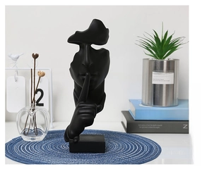 Close-up of matte black abstract face sculpture on blue woven mat in a modern home setting