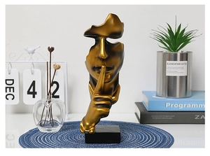 Close-up of a golden Silence is Gold resin sculpture on a blue woven mat in a home setting