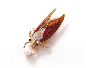 Macro shot of gold cicada brooch with red enamel, sparkling rhinestones and white pearl