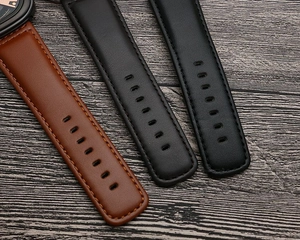 Close-up of brown and black leather watch straps with stitching on dark wood background