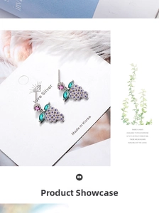 Detailed view of grape-shaped crystal earrings with green leaves on white display card
