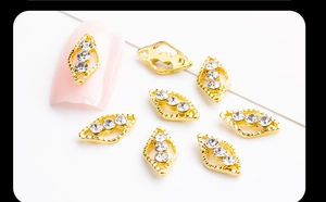 Macro view of gold rhombic nail charms with three sparkling rhinestones on manicured nail