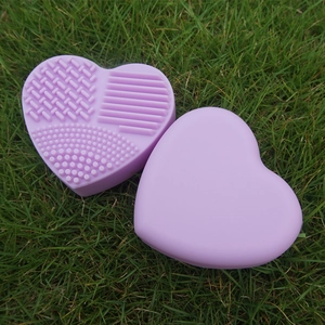 Macro shot of purple heart-shaped silicone makeup brush cleaning mat on green grass