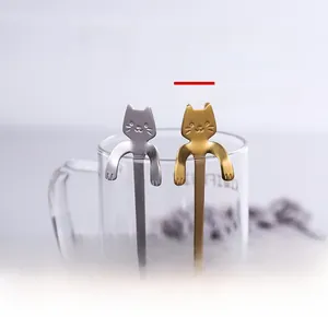 Detail of silver and gold cat-shaped stainless steel spoons hanging on a glass rim