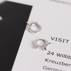 Macro detail of silver punk rivet hoop earrings with sparkling white zircon stones