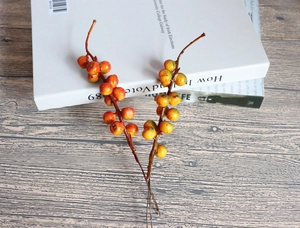 Detail of faux orange and green berry stems on a rustic gray wooden tabletop