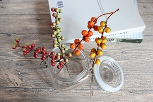 Close-up of artificial orange and red berries in a glass jar on a wooden desk