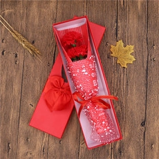 Detail of red carnation soap flowers in a gift box with a red ribbon on wood