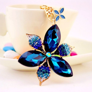 Porte-clés fleur en cristal bleu avec strass brillants et finition dorée sur fond blanc