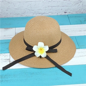 Women's summer straw sun hat with plumeria flower and brown ribbon on beach background