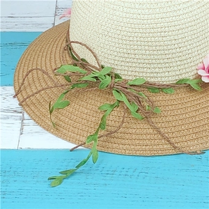 Straw sun hat with wide brim, featuring woven pink flowers and green leaves on beige fiber