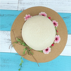 Wide brim straw sun hat with floral wreath decoration on a rustic blue wood surface