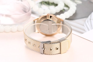 Détail du bracelet de montre en maille milanaise dorée et boîtier sur fond élégant rose