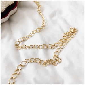 Detail of high-polish gold metal chain strap with classic twist links on a white sequin bag