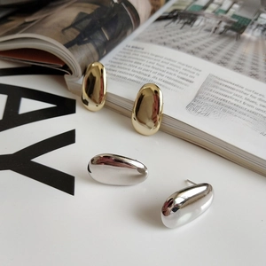 Minimalist oval metal stud earrings in gold and silver finish on a magazine background