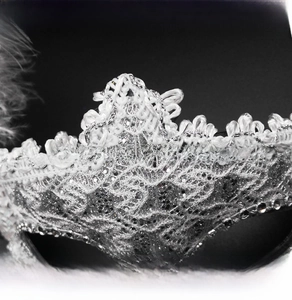Detail of white lace masquerade mask with silver sequins and feather accents
