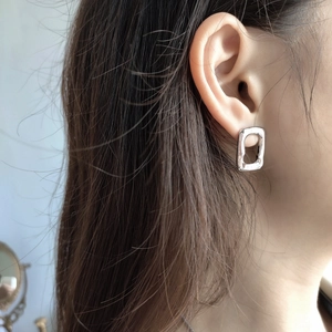 Close-up of minimalist silver rectangular stud earring worn on ear for size perspective