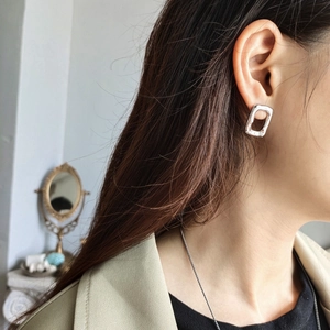 Close-up of a model wearing a geometric rectangular silver earring in a minimalist style