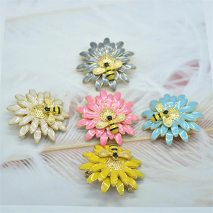 Daisy and honey bee enamel brooches in five colors on a soft white feather background