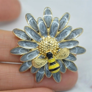 Close-up of enamel daisy flower brooch with a gold bee detail held between fingers