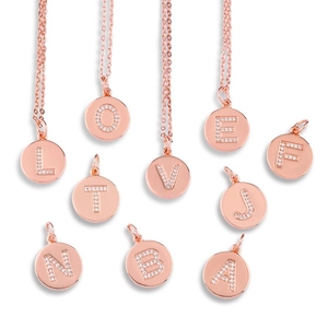 Detail of rose gold round alphabet pendants with micro-set zircons on a white background