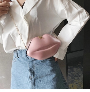 Detail of pink lip-shaped crossbody bag with gold chain strap worn by a model