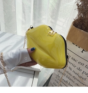 Detail of creative bright yellow lip-shaped bag in patent leather with gold chain strap