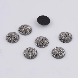 Detailed view of 14mm silver sparkling resin flatback cabochons with one showing the black base