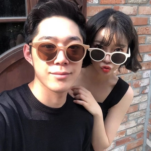 Retro round tea-colored and off-white sunglasses worn by a couple on a brick wall background