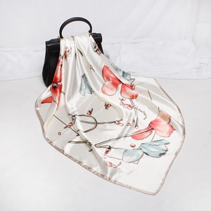 Detailed view of elegant floral silk scarf tied to a black leather handbag handle