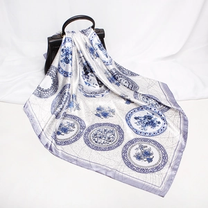Blue and white porcelain print silk square scarf draped over a dark leather handbag