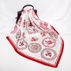 Elegant silk scarf with red floral patterns draped over a stylish black handbag