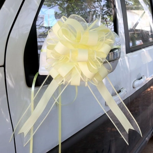 Pale yellow decorative bow on a white car mirror featuring pearl ribbon and soft mesh layers