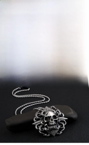 Detail of gothic stainless steel skull pendant with vintage engraved relief on dark stone