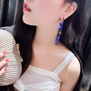 Close-up of model wearing long rectangular drop earrings with dark blue crystals