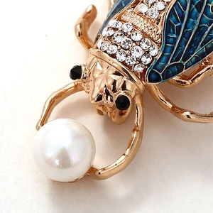 Detailed macro shot of beetle brooch with blue enamel wings and a white pearl