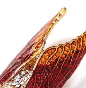 Detail of a handmade cicada brooch with red-orange enamel wings and sparkling rhinestones