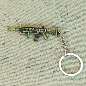 Detailed close-up of a vintage brass rifle miniature keychain on a textured fabric surface