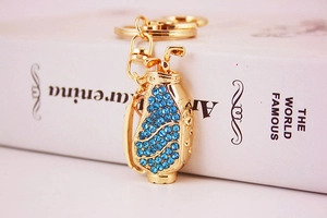 Macro view of a gold golf bag keychain featuring sparkling blue rhinestones on a white book