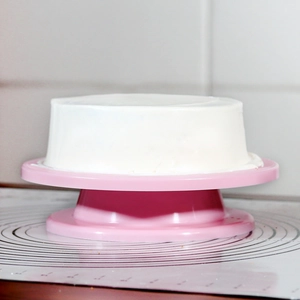 Pink revolving cake turntable with white cream cake on a scale silicone mat