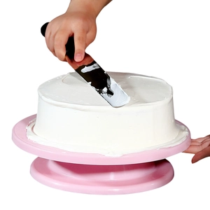Action shot of a stainless steel cake spatula smoothing cream on a pink rotating turntable